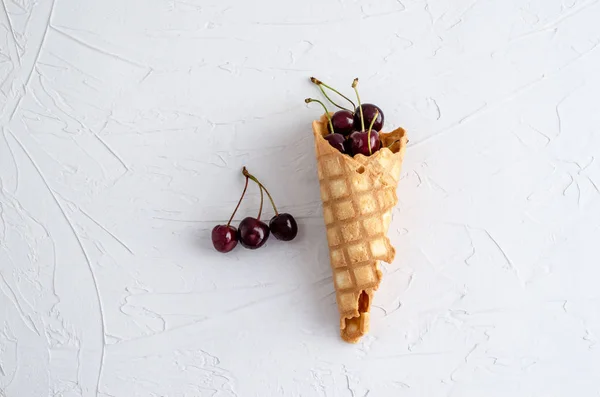 Конус мороженого с вишнями на белом бетоне — стоковое фото