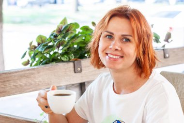 Kırmızı saçlı genç bir kız siyah c bir fincan ile bir masada oturur