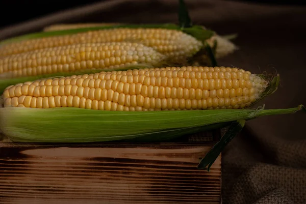 Yellow sweet raw corn in a wooden box on textile background clos — Stock Photo, Image