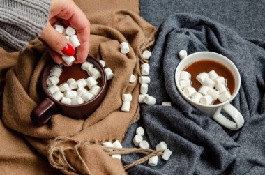 A female hand adds white marshmallows to brown and white cups wi clipart
