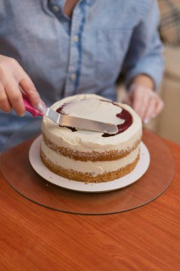 Pudra kek üzerine krema düzeyleri. Aşçı bir pasta oluşturur, topladığı ve krema ile kapsar ve bir spatula ve sıyırıcı ile düzeyleri.