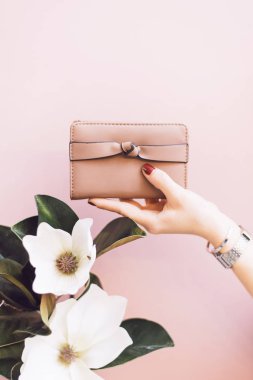 Kadın şık cüzdan pembe pastel arka plan üzerinde kırmızı manikür ile bir kızın elinde. Bir kızın elinde bir çiçek. Stil ve moda kavramı. Elinde çanta.
