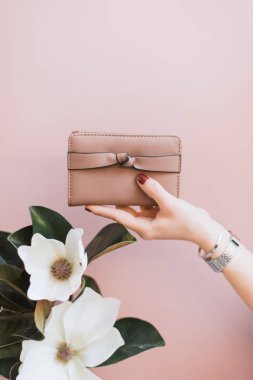 Kadın şık cüzdan pembe pastel arka plan üzerinde kırmızı manikür ile bir kızın elinde. Bir kızın elinde bir çiçek. Stil ve moda kavramı. Elinde çanta.