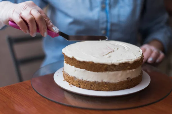 Girl Pastry Chef, makes a wedding cake with his own hands and squeezes the cream on the cake layers. Copy space. Selective focus.A confectioner makes white cream using a spatula for cooking. Line the cream on the cake.