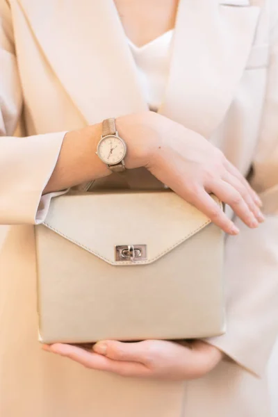 bag in hand. Vertical photo of a girl with a gold bag in her hands and watches. Beige suit