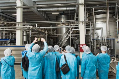 excursion at the factory. People in protection, shoe covers, blue overalls stand and listen to a tour of the metal brewery. People Photograph production on the phone clipart