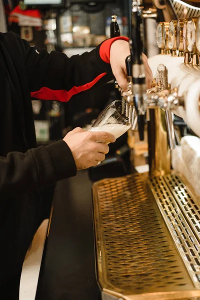 bartender hands pouring beer from the tap in the bar. A man pours a frothy drink. Golden tap and bar counter. Chilled drink in the tap with ice