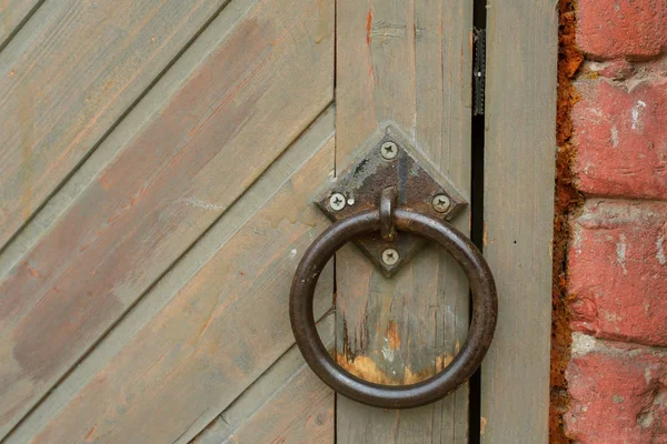 An old vintage door handle ring on a wooden door. The shutter is on the brown door. Round metal handle. Horizontal photo