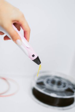 çıplak manikür ile kız sarı bir plastik çubuk ile 3d kalem çizer. Plastik bobin ile beyaz bir arka plan üzerinde 3d kalem