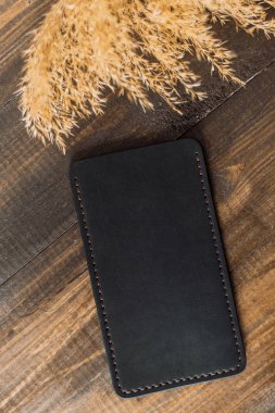 Ahşap ve buğday bir arka plan üzerinde eko-deri pahalı, güzel kapak. Güzel doğa bakım konsepti. Siyah renkli el yapımı telefon kılıfı
