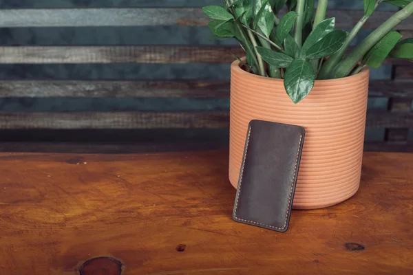 Manly leather phone case on wooden background. Next to the aksusekar is a potted flower