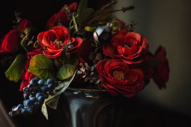 Bir vazo masada Gotik buket. Karanlık bir arka planda kırmızı güller, mavi çiçekler koyu buket.