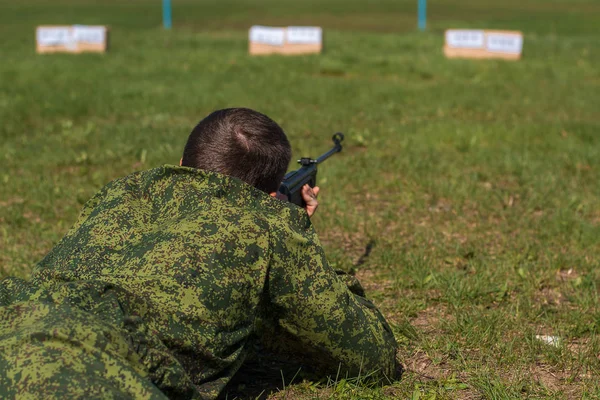 A man is aiming at a target. Sniper lies on the grass and shoots from a machine gun.