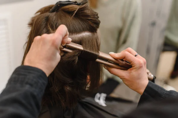 Hairdresser curls hair with a hair straightener. Master creates a hairstyle girl.