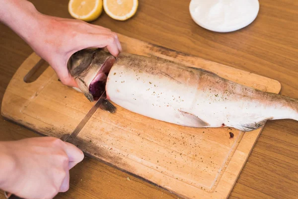 A woman prepares fish, cutting fish on a wooden board, the cook season the trout