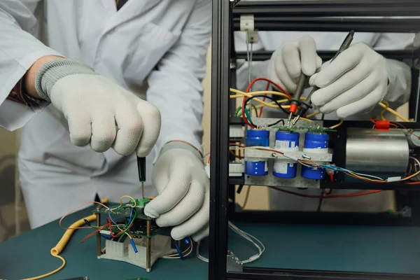 workers in gloves assemble an electrical circuit and measure the voltage