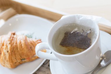 sıcak su bir fincan demlenmiş çay poşeti. Kruvasan ile lezzetli kahvaltı