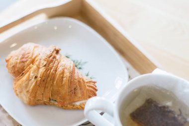 Ahşap masada somon ve yeşil ot ve çay ile Kruvasan.