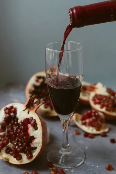 Rødvin med åpent granateple på en teksturert grå betongbakgrunn. En mann heller rødvin fra en flaske over i et glass . – stockfoto