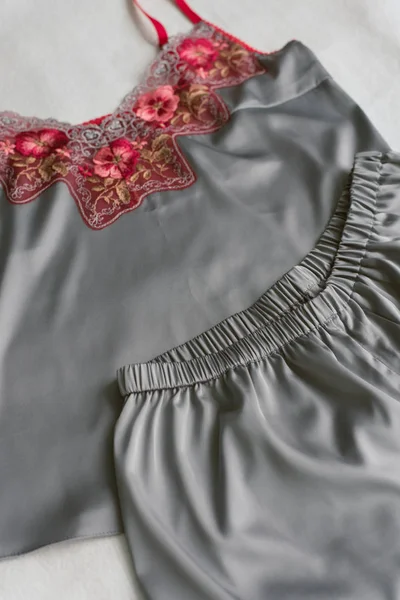 Pijama de seda hecho en casa acostado en la cama sin nadie. pijama gris con encaje rojo sobre fondo beige . — Foto de Stock