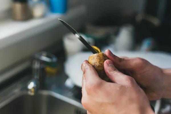 Homem limpa batatas com uma faca na pia em casa. descasque batatas pequenas. limpeza na pia . — Fotografia de Stock