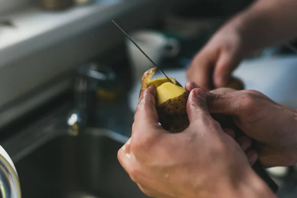 El hombre limpia papas con un cuchillo en el fregadero de casa. pelar patatas pequeñas. limpieza en el fregadero . — Foto de Stock