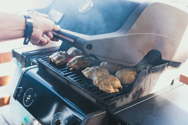 Grilled chicken at a picnic. The man laid the chicken in the marinade on the grill for its preparation. Entire large carcasses of hens are on fire. to cook outside. man closes the grill — Stock Photo, Image