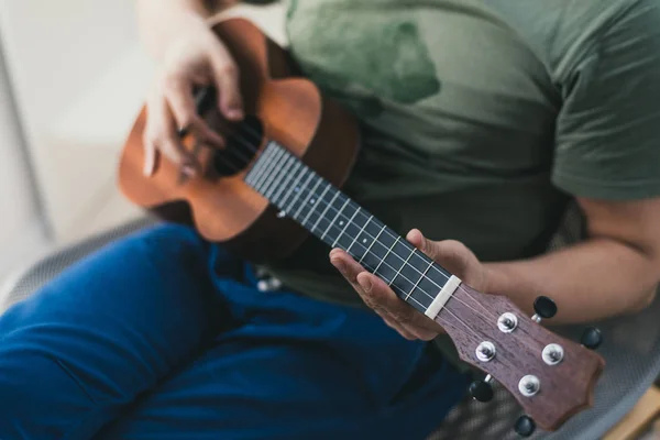 Jogo de ukulele. um homem a tocar guitarra. o intérprete escreve a música no ukulele em casa . — Fotografia de Stock