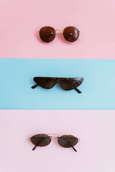 Three sunglasses on a pink and blue pastel background. The concept of summer and stylish vacation. — Stock Photo, Image