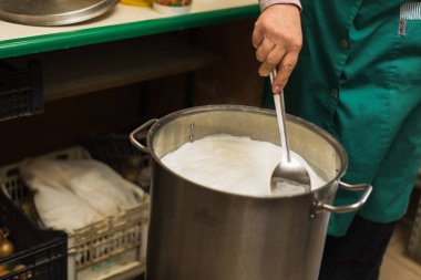 Evde süzme peynir ve peynir pişiriyorum. Adam alüminyum tavada peynir, ısıtma sütü ve peynir altı suyu oluşturur.