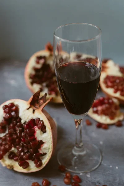 Um copo de vinho com vinho tinto fica em um fundo grunge cinza ao lado de granadas. Frutas e vinho de romã — Fotografia de Stock