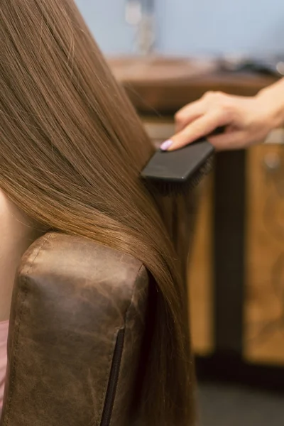 La chica de la peluquería peinaba. Morena en el salón de belleza alisar y peinar su cabello . —  Fotos de Stock