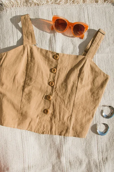 Καφέ μπλούζα από λινό με ξύλινα κουμπιά και γυαλιά ηλίου με ασημένια σκουλαρίκια σε μπεζ χαλί. — Φωτογραφία Αρχείου