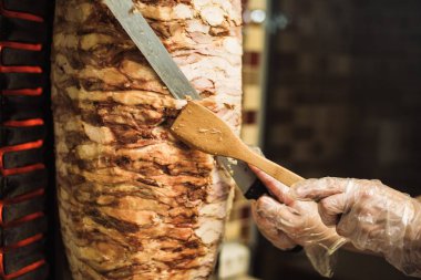 Bir kafede shawarma ve ciabatta pişirmek. Tek kullanımlık eldivenli bir adam şişte et keser..