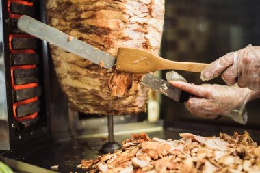 Bir kafede shawarma ve ciabatta pişirmek. Tek kullanımlık eldivenli bir adam şişte et keser..