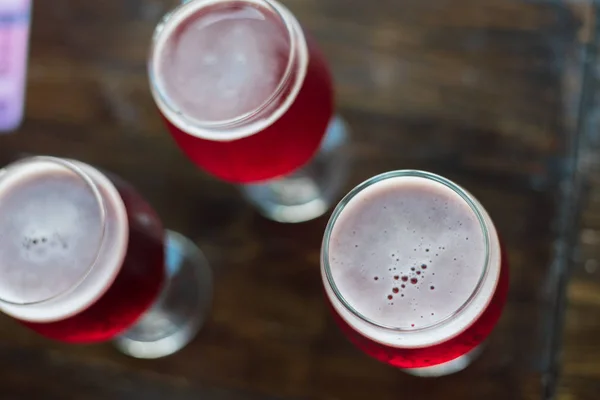 Three glasses with red wine on a wooden table. Glasses of cherry beer are on the table. There is no one in the frame. — Stock Photo, Image