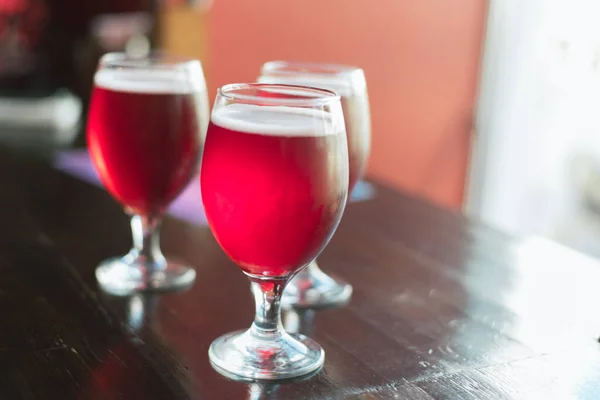 Três copos com vinho tinto numa mesa de madeira. Copos de cerveja cereja estão sobre a mesa. Não há ninguém no quadro. . — Fotografia de Stock