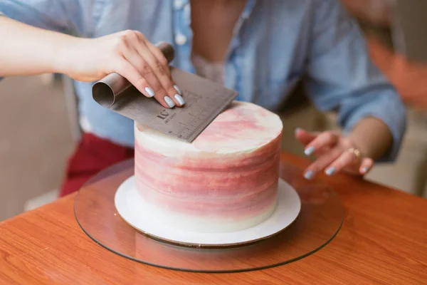 빵집에서 케이크를 만드는 사랑스러운 소녀. 소녀는 케이크에 크림을 부드럽게. 나무 테이블에 흰색 케이크. — 스톡 사진