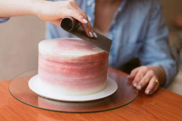Милая девушка делает торт в пекарне. Девушка разглаживает крем на торте. Белый торт на деревянном столе . — стоковое фото