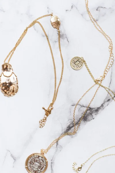 Pingentes de ouro na moda e na moda e ornamentos com conchas e moedas em um fundo de mármore. jóias elegantes . — Fotografia de Stock