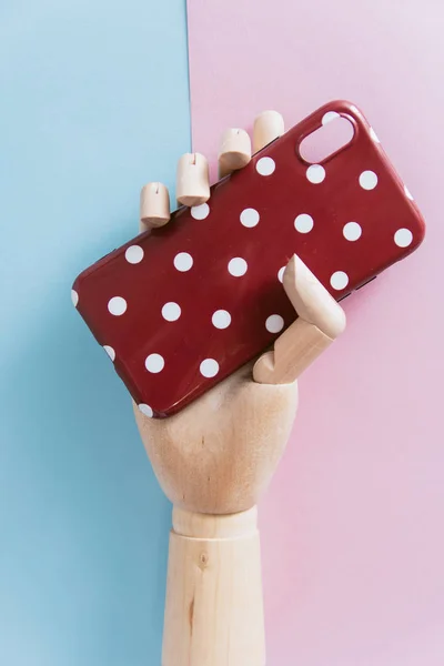 Kleur mooie cover in de hand van het meisje op een roze en blauwe pastel achtergrond. telefoon geval in de scharnierende houten hand — Stockfoto