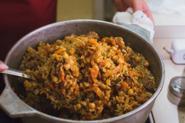 Kazanda mutfakta oryantal pilav pişirmek. Bir kadın kuzu, sığır eti, pirinç, nohut, havuç bir tabak hazırlar