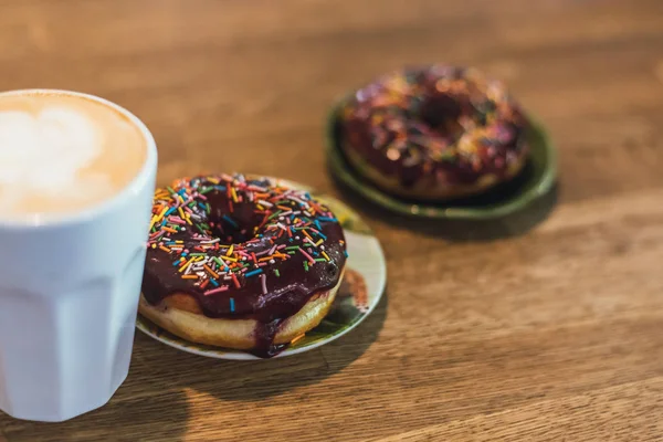 Coffee with a drawn heart and milk on a wooden table in a coffee shop. two chocolate donuts with scattering on the table next to the coffee