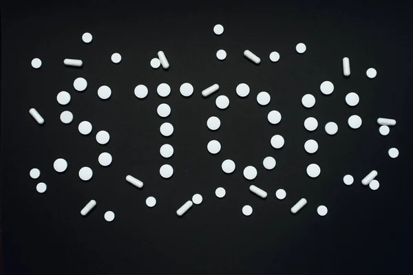 Word Stop hecho de píldoras blancas sobre un fondo negro. El concepto de adicción a las drogas, píldoras y sedantes. Adicción farmacéutica — Foto de Stock