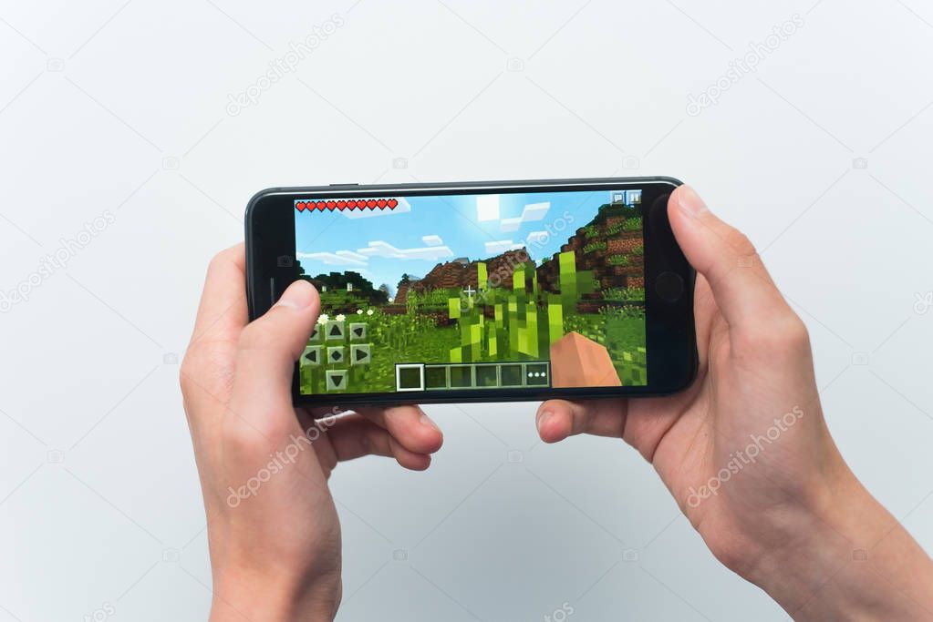 Samara, Russia -07, 29, 2019: A young guy playing minecraft game on Iphone 8 Plus. Teenage boy holding a phone in his hands with a game minecraft on a white background.