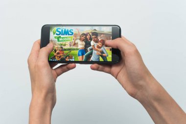 Samara, Rusya -07, 29, 2019: Genç bir adam Iphone 8 Plus bir Sims oyunu oynar. Genç çocuk beyaz bir arka plan üzerinde bir oyun Sims mobil ile elinde bir telefon tutarak