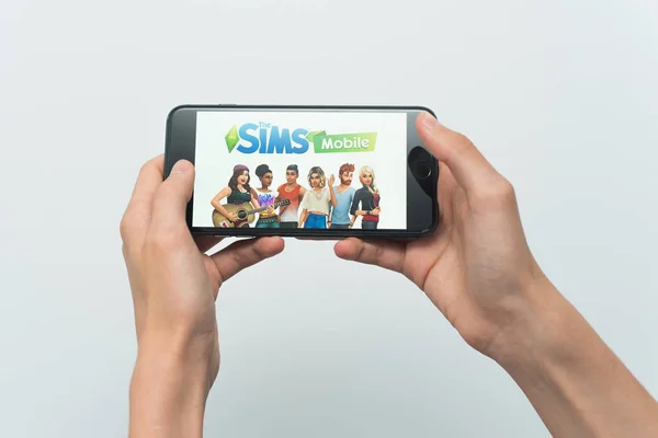 Samara, Russia -07, 29, 2019: Un joven juega un juego SIMS en Iphone 8 Plus. Adolescente sosteniendo un teléfono en sus manos con un juego Sims móvil sobre un fondo blanco — Foto de Stock