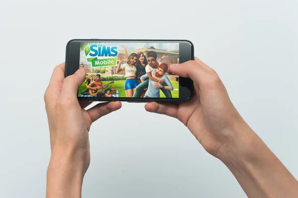 Samara, Russia -07, 29, 2019: A young guy plays a SIMS game on Iphone 8 Plus. Teenage boy holding a phone in his hands with a game Sims mobile on a white background — Stock Photo, Image