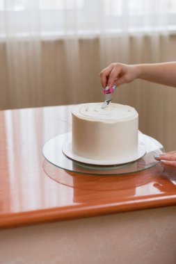 Kız kremayı pastanın üzerine sıkıştırıyor. Fırında pasta yapan sevimli bir kız. Kız pastanın üzerindeki kremayı yumuşa. Ahşap bir masada beyaz kek.