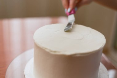 Kız kremayı pastanın üzerine sıkıştırıyor. Fırında pasta yapan sevimli bir kız. Kız pastanın üzerindeki kremayı yumuşa. Ahşap bir masada beyaz kek